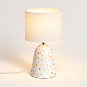 Lámpara de mesa de cerámica blanca con lunares y pantalla de lino, luz encendida