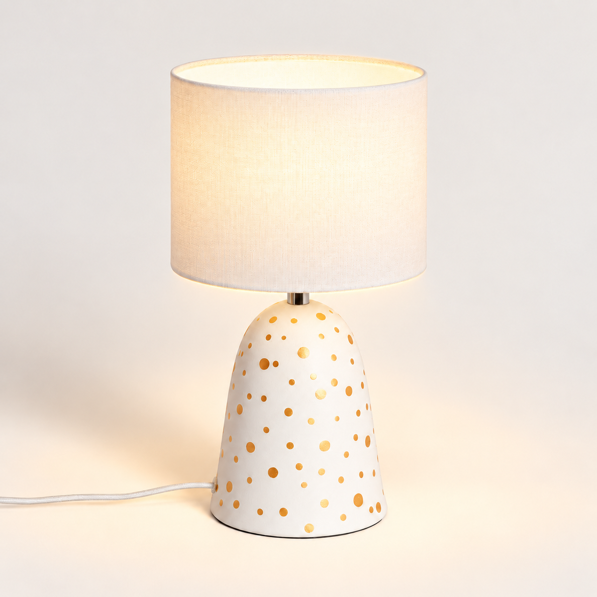 Lámpara de mesa de cerámica blanca con lunares y pantalla de lino, luz encendida