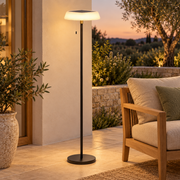 Lámpara de pie solar negra encendida en una terraza exterior, con panel superior y tirador