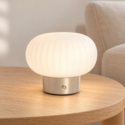 Lámpara de mesa LED níquel encendida sobre mesa de madera en interior claro