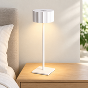Lámpara de mesa recargable blanca con pantalla facetada encendida sobre una mesilla