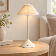 Lámpara portátil beige con pantalla plisada encendida sobre una mesa auxiliar