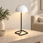 Lámpara blanca y negra encendida con base tubular abierta en un ambiente interior claro