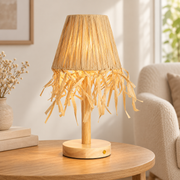 Lámpara de madera y rafia natural encendida en una mesa auxiliar de interior