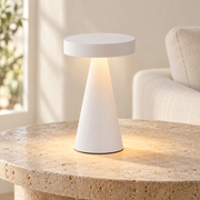 Lámpara de mesa blanca de disco y base cónica encendida sobre una mesa clara