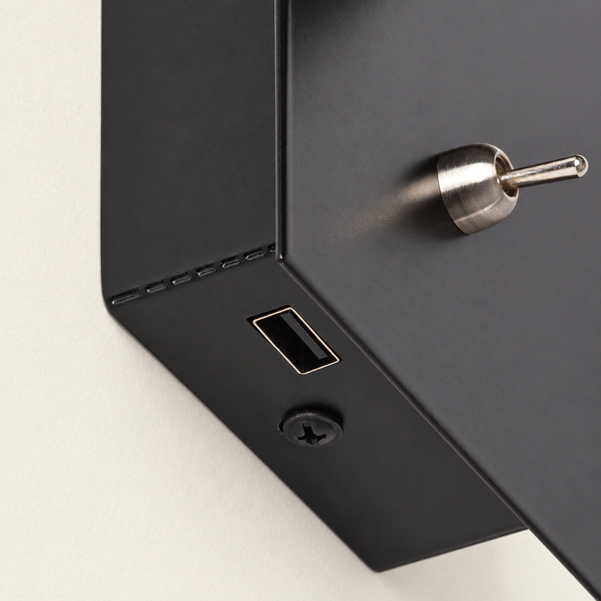 Detalle del único puerto USB-A inferior y tornillo negro del aplique, con interruptor de palanca frontal